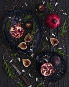 Fresh cut figs and pomegranates placed on plates near arugula and knife on lumber table