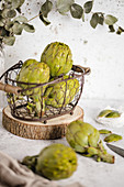 Bright green artichokes in metal stylish basket decorated with green leaves on table
