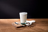 Glass of fresh milk on wooden board with spoon and coffee grains