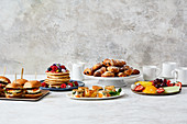 A breakfast buffet with burgers, pancakes, pastries and fruit