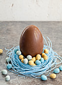 Large chocolate Easter egg, sitting in a blueberry candy nest, filled with mini chocolate eggs