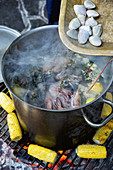 Seafood in a saucepan and corn cobs on a grill