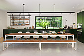 Long dining table, bench and chairs in front of dark green kitchen counter