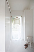 Romantische Bluse hängt im Fenster mit Gardine im weißen Raum