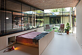 Pull-out bed in guest room in front of glass wall with view of inner courtyard