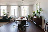 Open-plan living-dining area with wooden table, black chairs and indoor plants