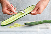 A cucumber being deseeded with a teaspoon