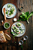 Bread with wild garlic pesto, cream cheese and cucumber on a wooden background