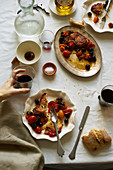Overhead image of family dinner table with roasted fish, tomatoes, olives and wine