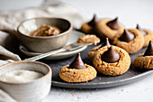 Peanut butter in a pinch bowl on a dark grey plate surrounded by chocolate kisses cookies