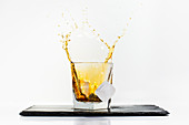 Glass of yellow cold drink with falling ice cube and splashes