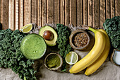 Glass of green healthy vegan smoothie, glass straw, Kale, bananas, avocado, lime, non-diary milk, matcha powder and seeds