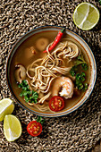 Asian spicy noodles soup with shiitake mushrooms and prawns, ingredients above on straw wicker napkin as background