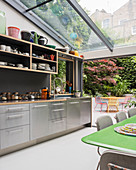 Modern kitchen and dining table below glass ceiling with garden access in background