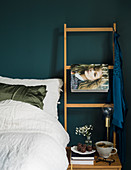 Weiß bezogenes Bett vor taubenblauer Wand mit Holzleiter und Modezeitschrift
