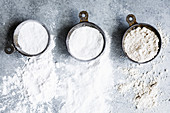 Three types of flour in measuring cups on a gray background