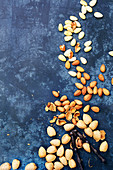 Almonds in shells, almonds kernals and blanched almonds scattered on a textured blue background.