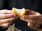 Frauenhände halten frittiertes Käsebällchen mit Mozzarellafüllung