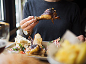 Crop unrecognizable man eating grilled chicken leg in fast food restaurant