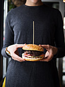 Crop anonymous person in black wear holding classic burger with cutlet and vegetables with cheese