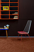 Metal chair below orange shelves on brown wall