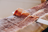 Knife cutting thin slice of ham with tallow lines