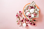 Bunch of delicate flowers arranged near plate with chicken eggs on Easter Day on pink background