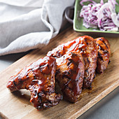 Yummy grilled chicken wings placed on wooden board near plate with chopped onion and napkin