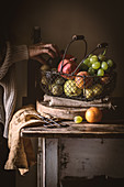 Unrecognizable elderly person taking ripe fruit from metal basket on rustic table