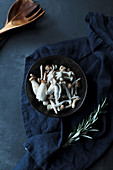 Uncooked mushrooms and fresh green rosemary stems on on dark blue towel