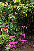 Hot-pink garden furniture below bunting hung in tree in garden