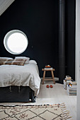 Bett unterm runden Fenster in schwarzer Wand im Schlafzimmer