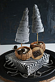 Two miniature fabric fir trees on zebra-patterned box against black background