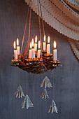 Suspended Advent wreath made from branches with lit candles and fir-tree pendants made from book pages