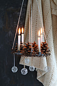 Suspended Advent wreath made from wire decorated with pine cones, wire balls and golden candles