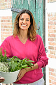 A young woman with a bowl of fresh herbs wearing a pink jumper