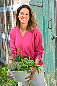 A young woman with a bowl of fresh herbs wearing a pink jumper