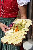 A woman wearing a dirndl serving a cheese platter with grapes