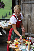 A woman wearing a dirndl at a breakfast buffet on an Alpine meadow