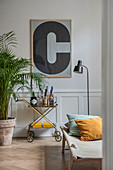 Large, framed letter C on wall above serving trolley against panelled wainscoting