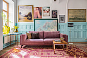 Purple velvet sofa against pale blue panelled wainscoting below gallery of pictures