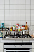Three pans on gas hob and canned groceries in white-tiled kitchen