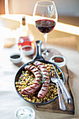 Sausages with Potatoes in a cast iron pan, Table served with glass of red wine