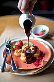 Profiteroles with melted chocolate pouring from saucepan and fruit