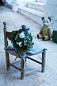 Vintage Kinderstuhl mit Weihnachtsgirlande und Teddybär im Hintergrund