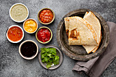Assorted Indian chutneys in rustic bowls and flatbread on grey concrete background