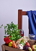 Fresh vegetables, fruit and herbs in a wooden crate on a chair