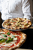 Kellner serviert Pizza Margherita und Pizza mit Artischocken und Culatello