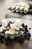 Weiße Kerzen im Teller mit Weihnachtskugeln und Kranz aus Zapfen
