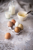 Hühnereier in einem Eierkarton, im Hintergrund Backzutaten